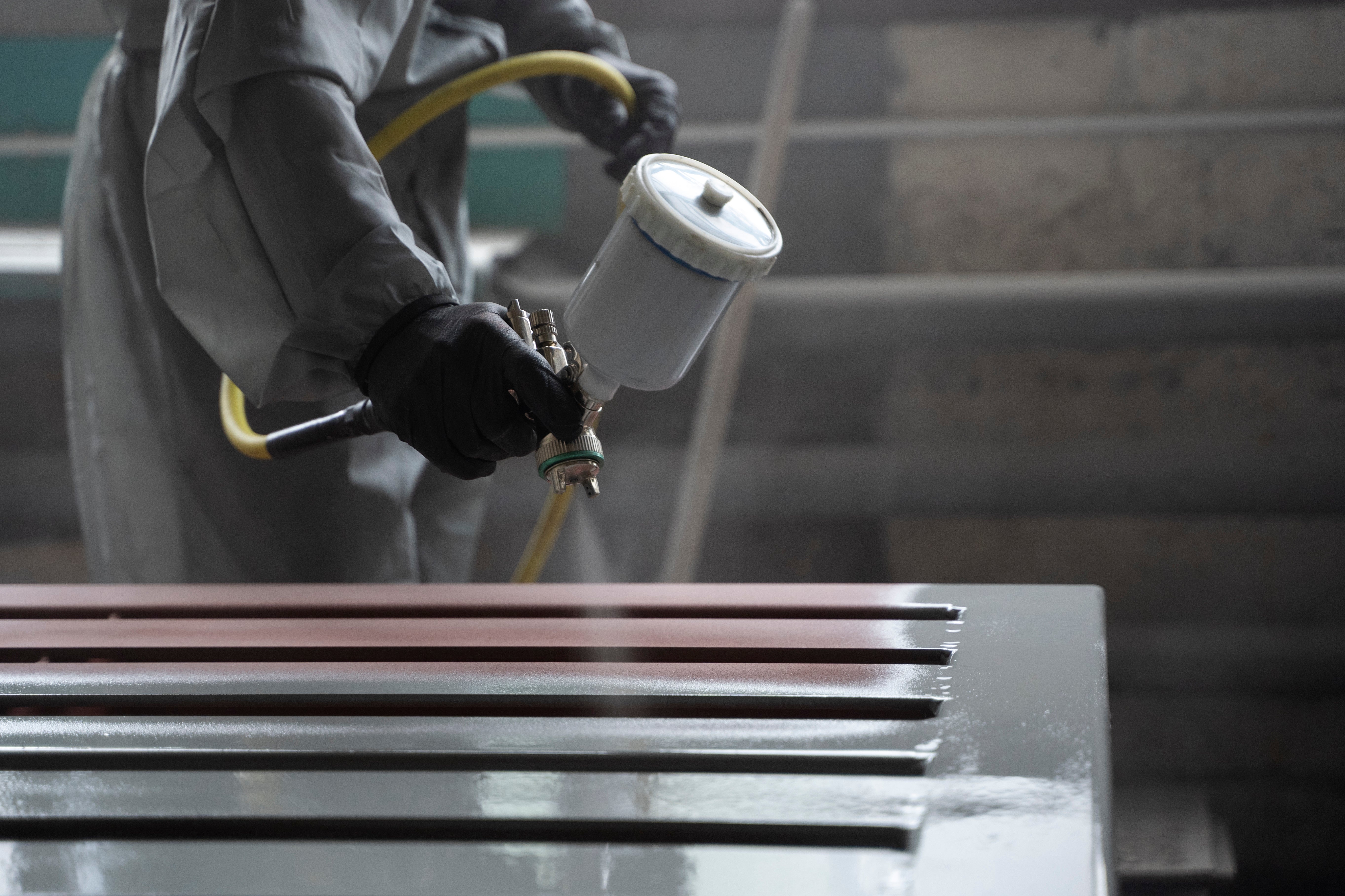Person spray painting a metal surface with a spray gun.