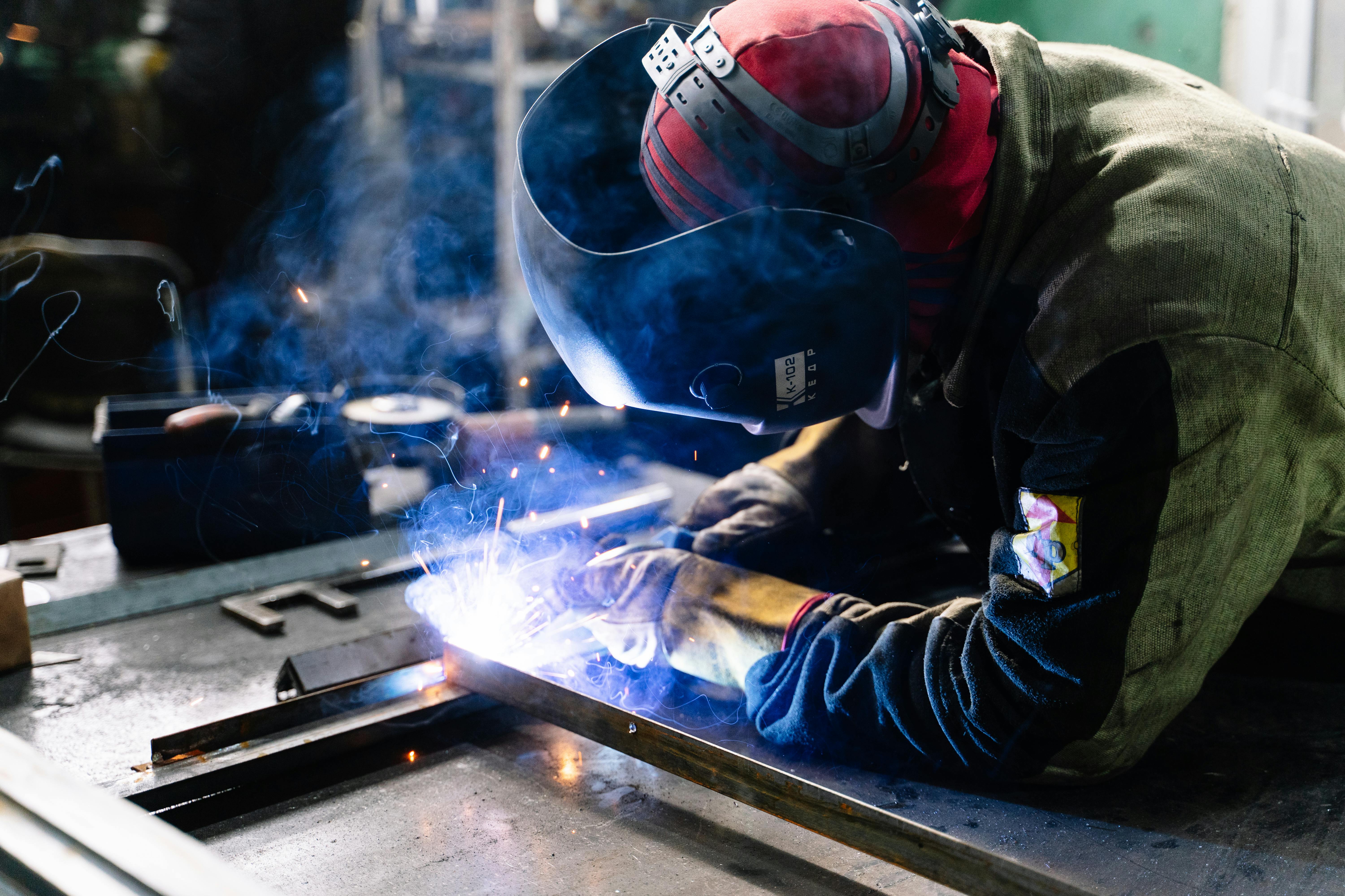 Person welding metal with protective gear in a workshop setting